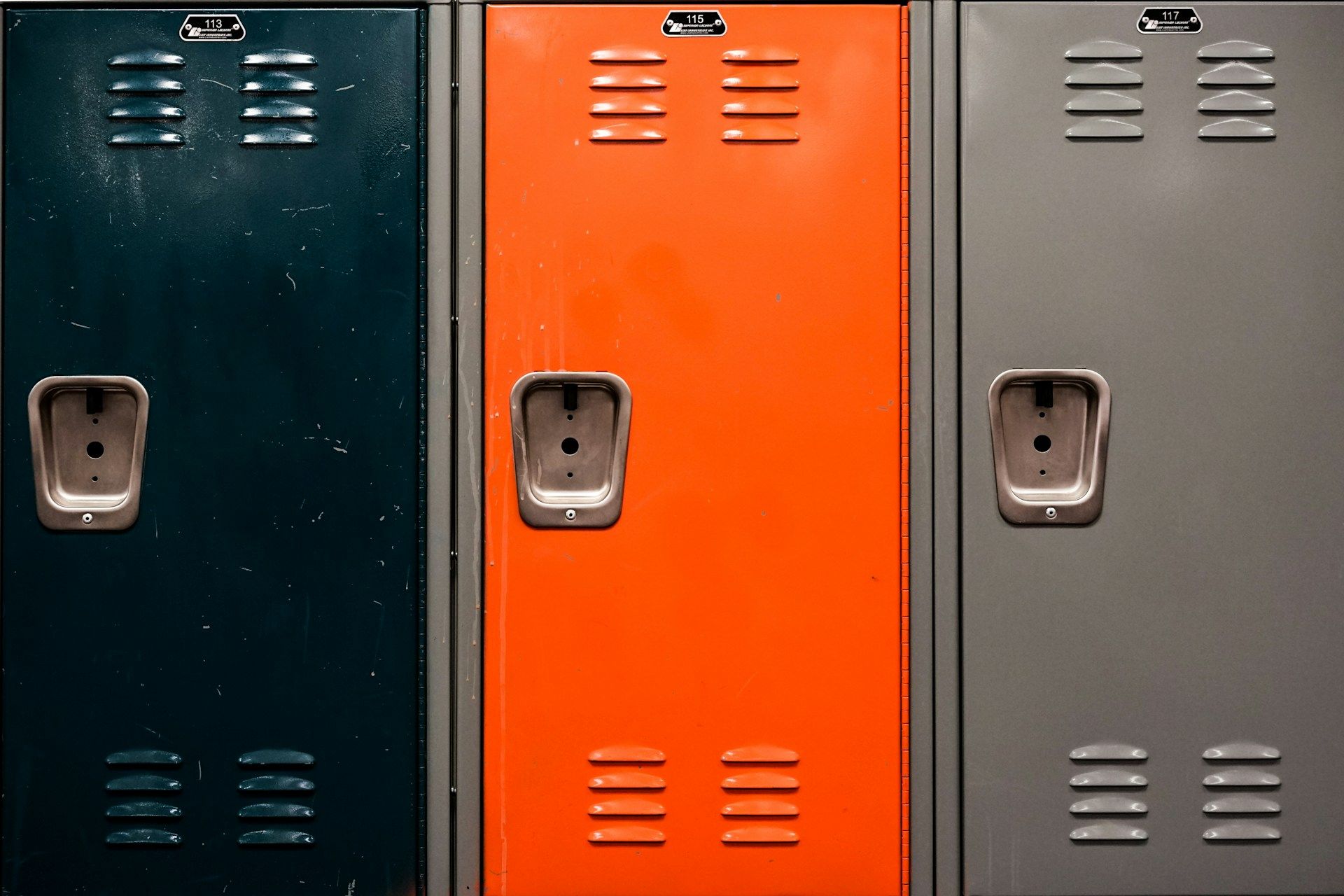 An orange school locker in between a black and gray locker